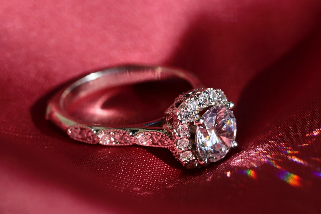 Light hits a vintage halo engagement ring that sits on red fabric.