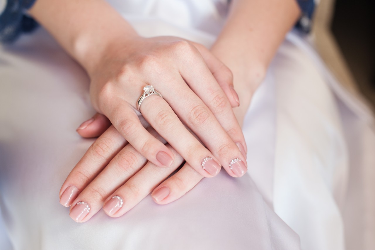 A bride sits with a solitaire ring on her finger, her hands crossed in her lap.