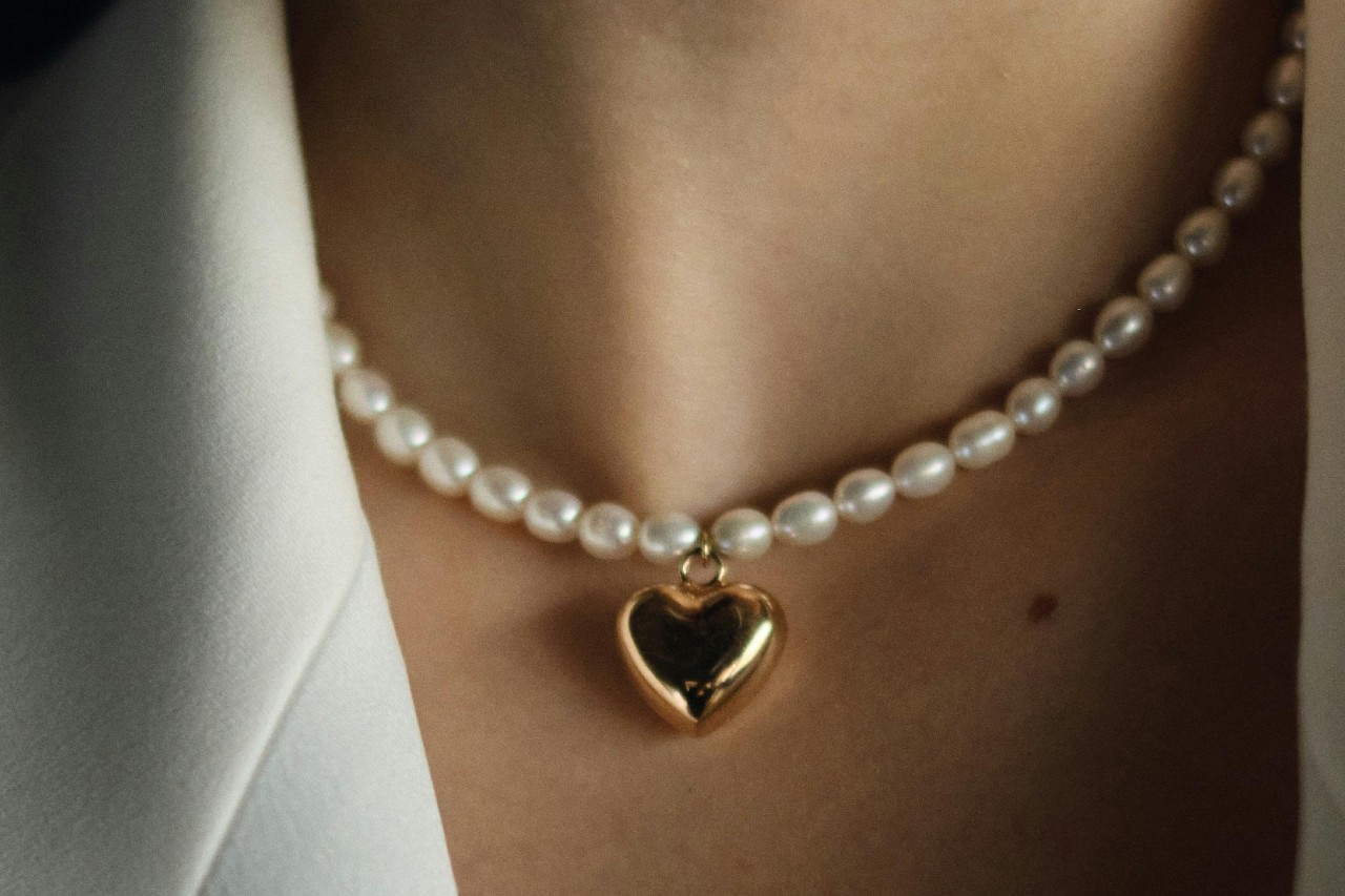 A close-up image of a woman’s neckline adorned with a pearl necklace with a heart pendant.