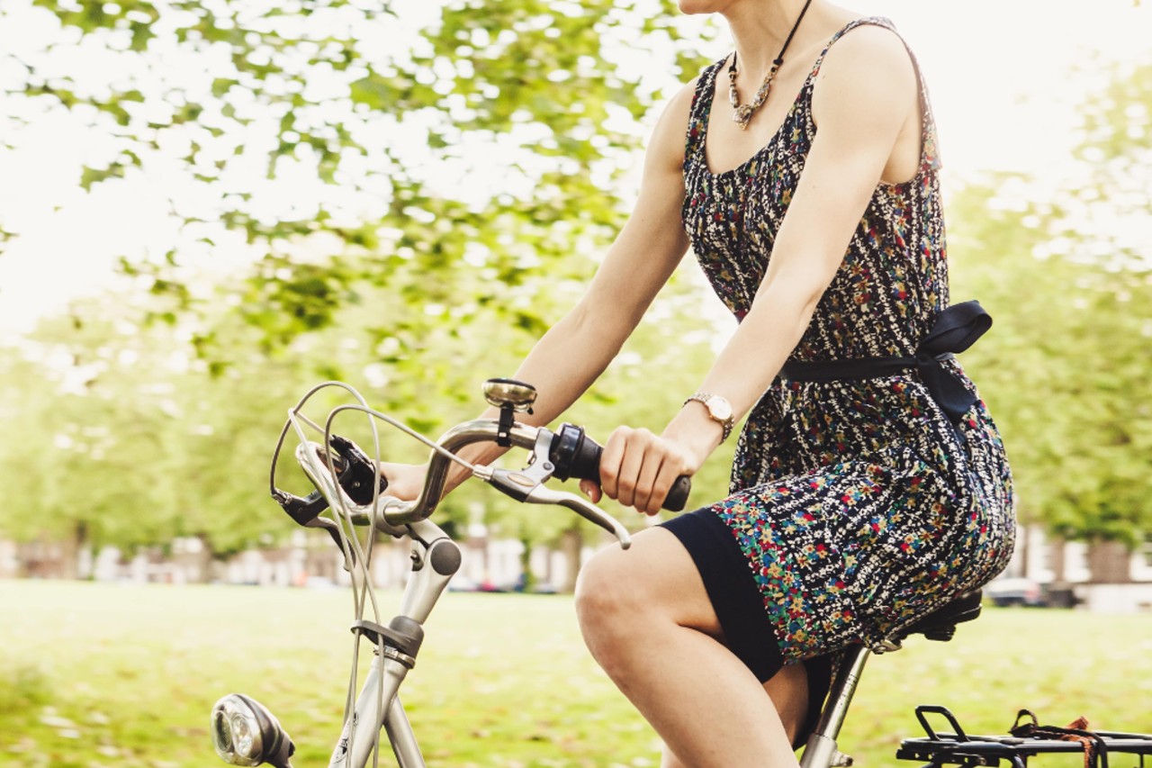 A close-up of a woman riding a bicycle, wearing an ornate necklace and complimentary watch.
