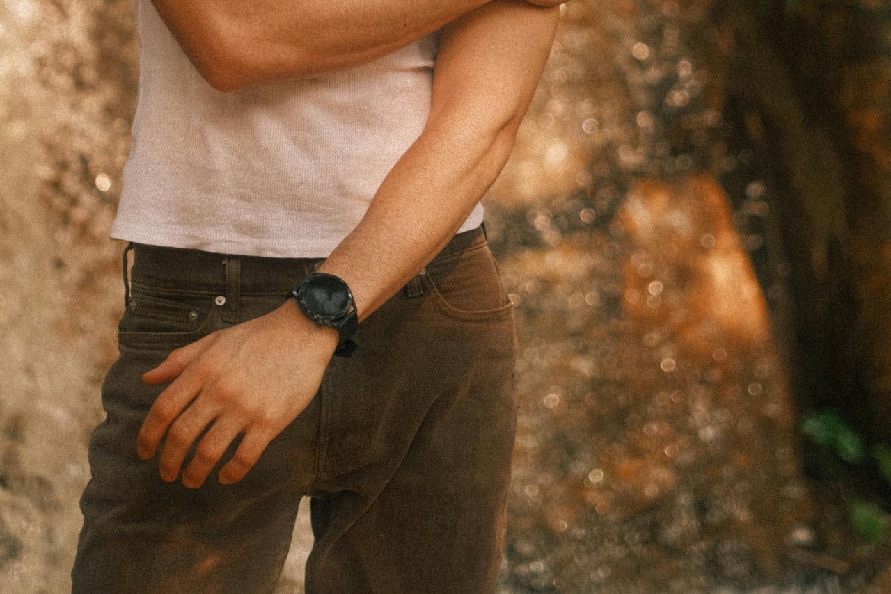 A close-up of a man in a white shirt and brown pants wearing a black sports watch.