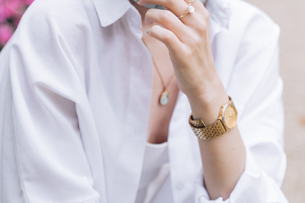 close up image of a woman wearing a white shirt and a gold watch with a gold dial