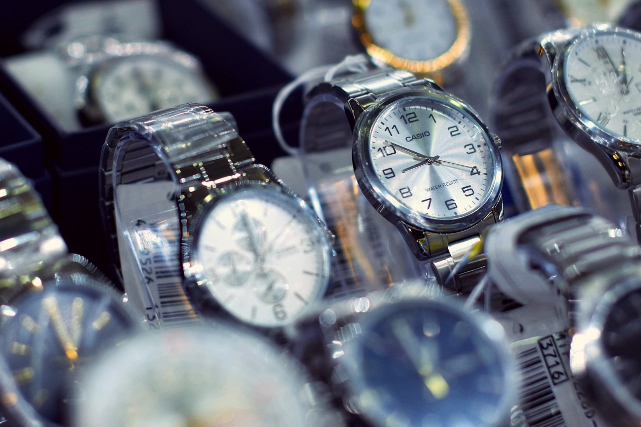 A display case filled with an assortment of wristwatches, focusing on a silver Casio watch with a white dial and bold black Arabic numerals.