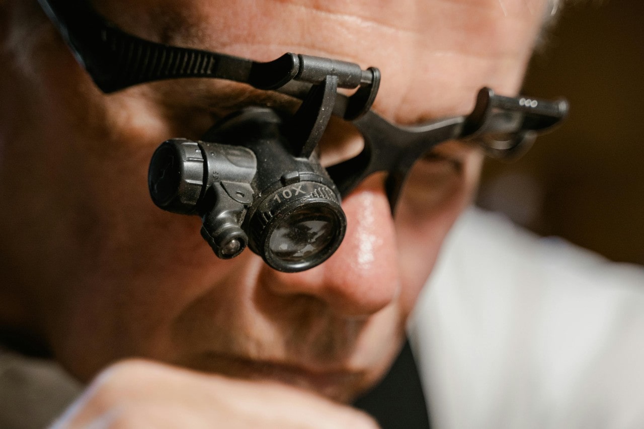 Close-up of a jeweler wearing a magnifying glass with a focused expression.
