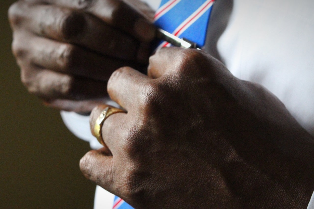 A groom adjusts his tie clip while wearing a yellow gold CrownRing wedding band A groom adjusts his tie clip while wearing a yellow gold CrownRing wedding band