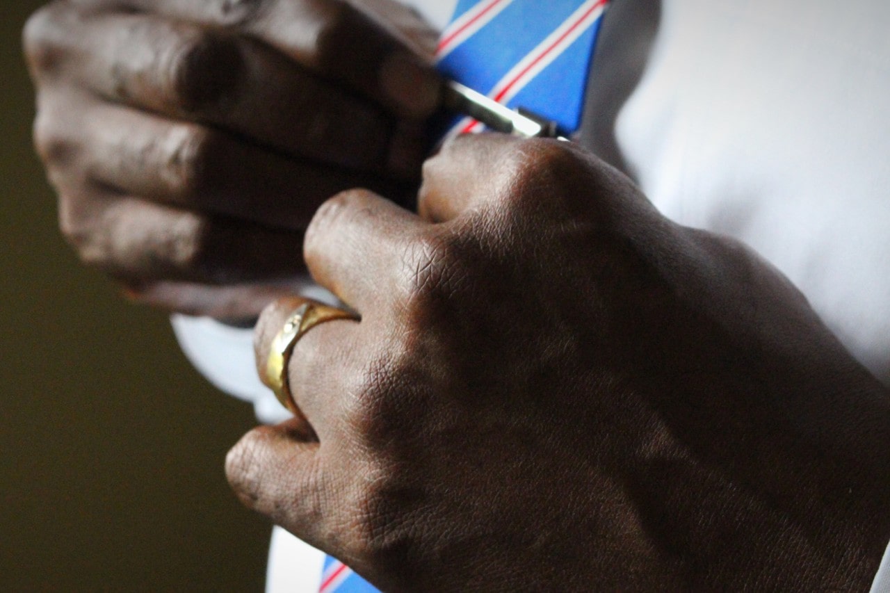 A groom adjusts his tie clip while wearing a yellow gold CrownRing wedding band