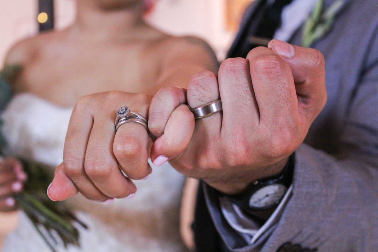 A newlywed couple linking pinkie fingers to show off their wedding bands after the ceremony