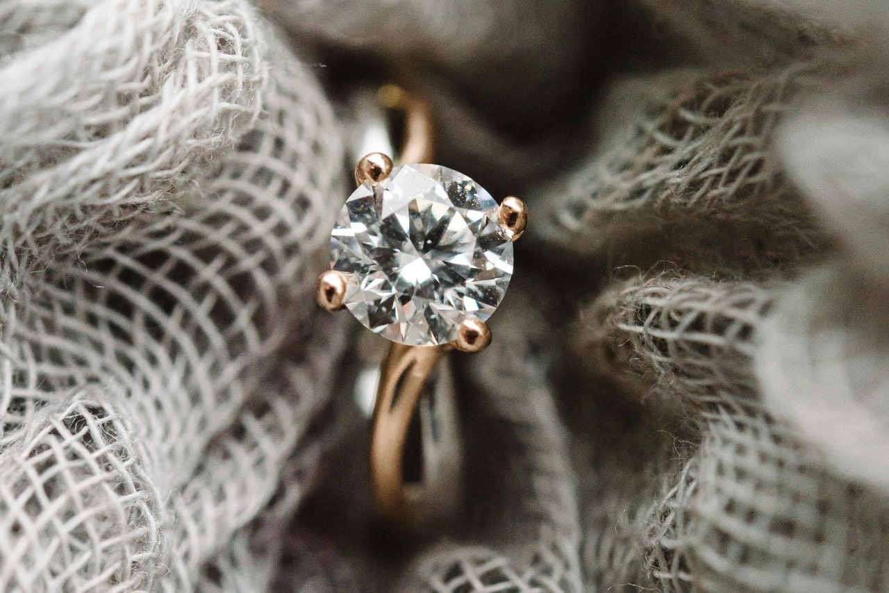 A close-up of a solitaire engagement ring delicately held in a piece of loose weave burlap. A close-up of a solitaire engagement ring delicately held in a piece of loose weave burlap.