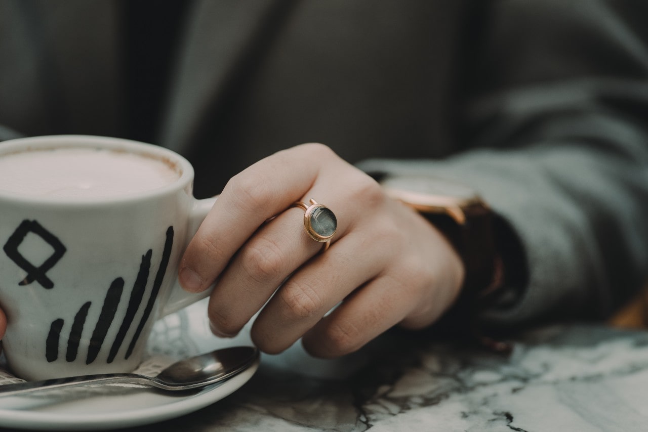 a hand holding a mug and wearing a fashion ring