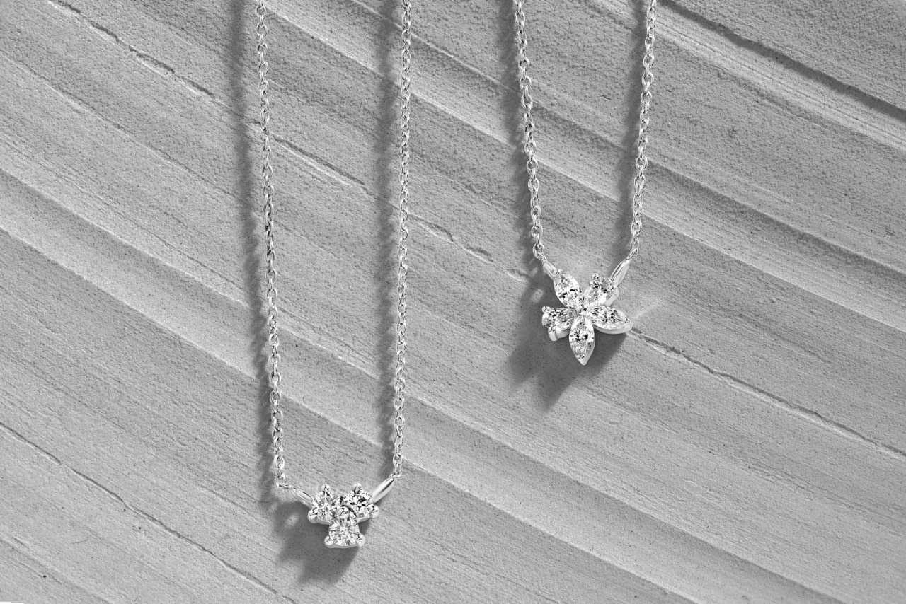 Two delicate diamond necklaces on a textured gray surface.