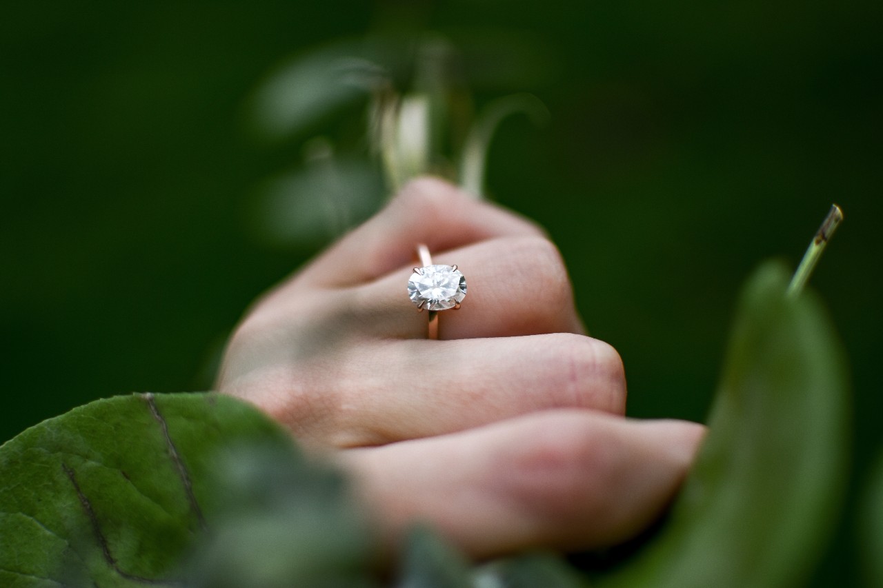 a woman holds a branch, wearing a solitaire oval-cut ring.