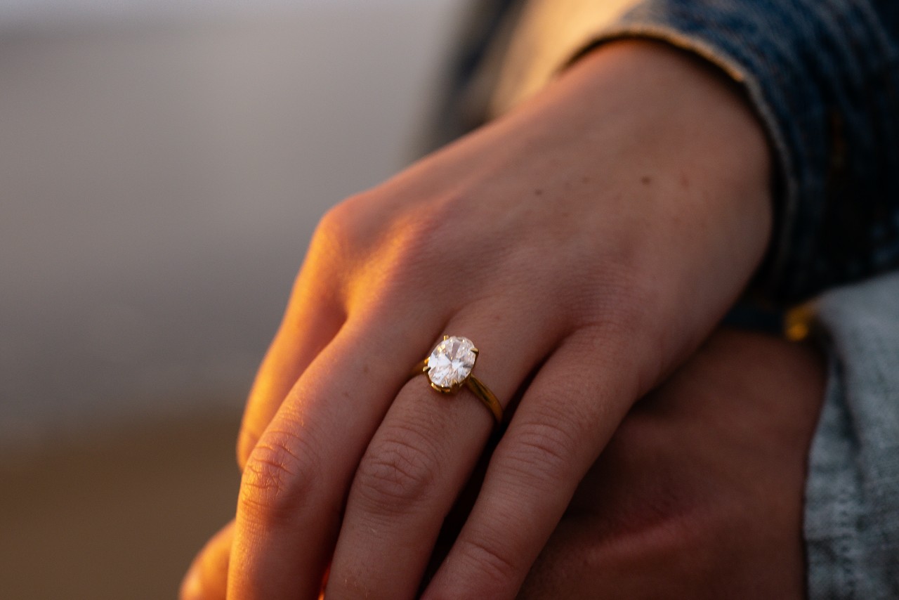 a woman holds her partner’s hand while wearing an oval engagement ring.