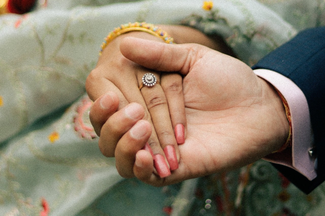 a man holding a woman’s hand who is wearing a halo engagement ring a man holding a woman’s hand who is wearing a halo engagement ring