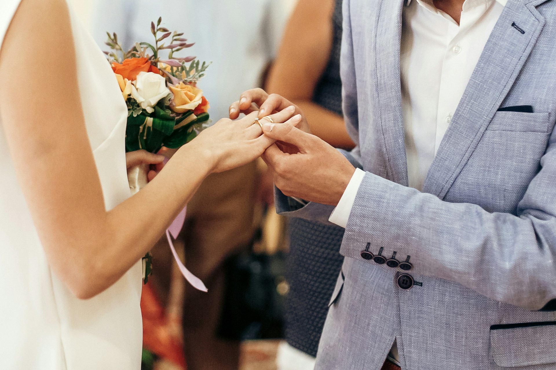 A close-up of a newlywed couple as the groom places a wedding band on the bride’s finger.