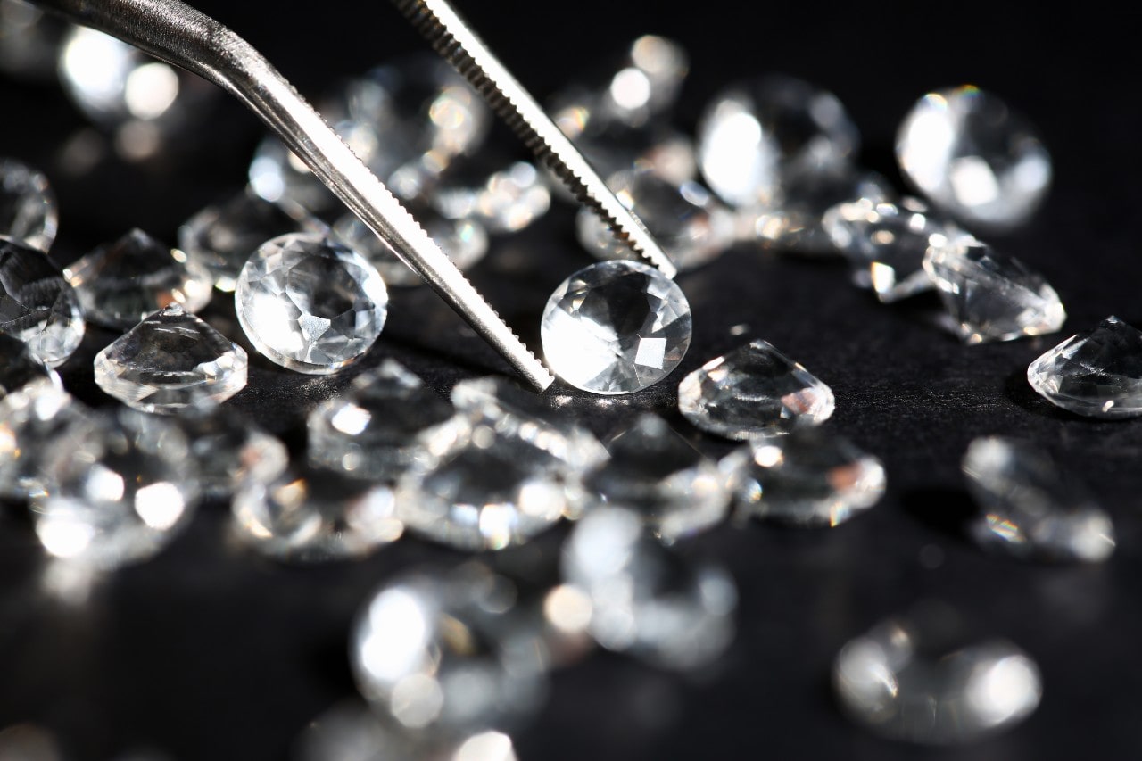 An assortment of round cut diamonds, one in a pair of jeweler’s tweezers