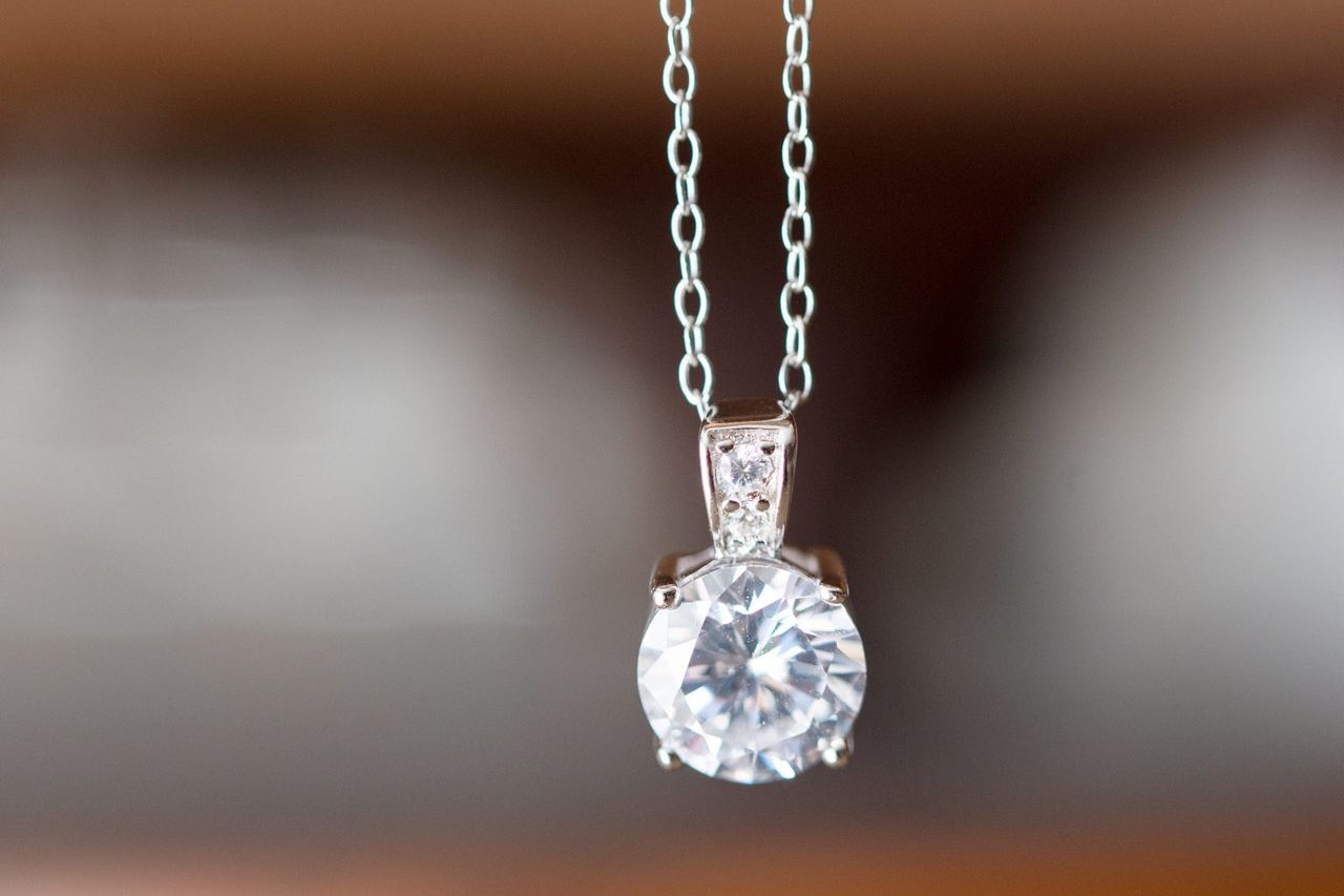 A prong-set round cut diamond is suspended by a sterling silver cable chain