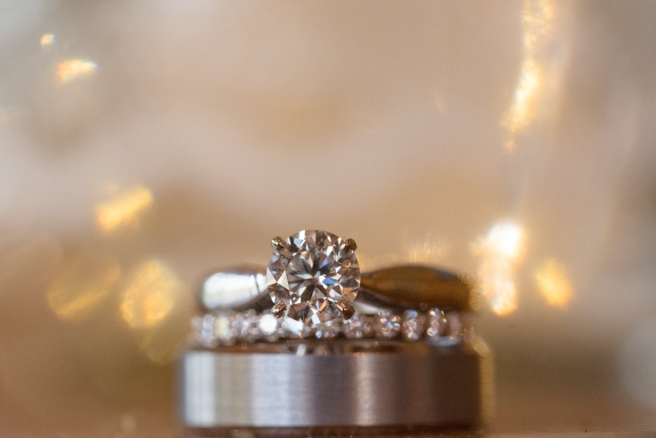 A platinum solitaire ring with a round-cut center diamond sits on top about two wedding bands