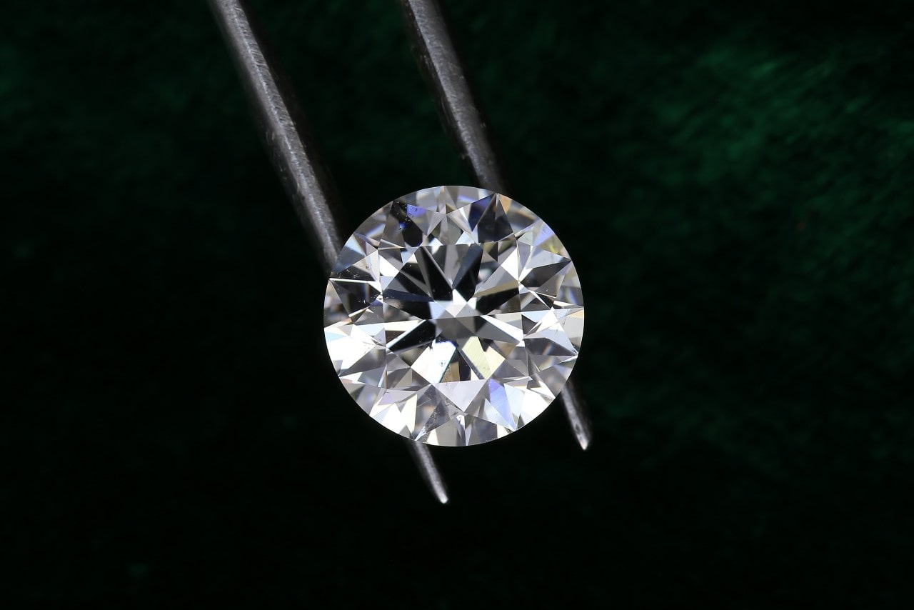 A single round diamond between the tweezers of a jeweler