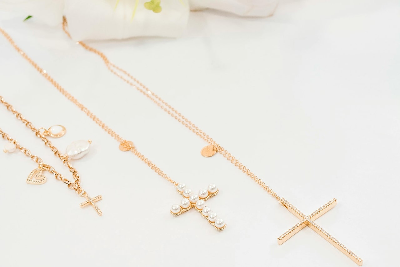 Three gold necklaces with cross pendants, some adorned with pearls and intricate details, while one is adorned with small diamonds, displayed on a white surface.