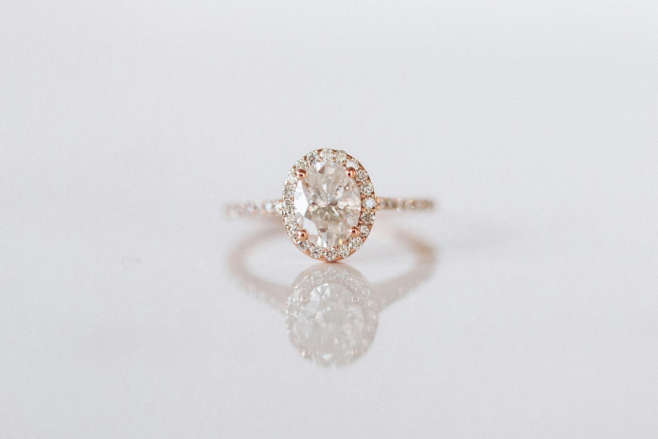 Elegant rose gold hidden halo ring with oval diamond center reflecting light on a soft, pale background.