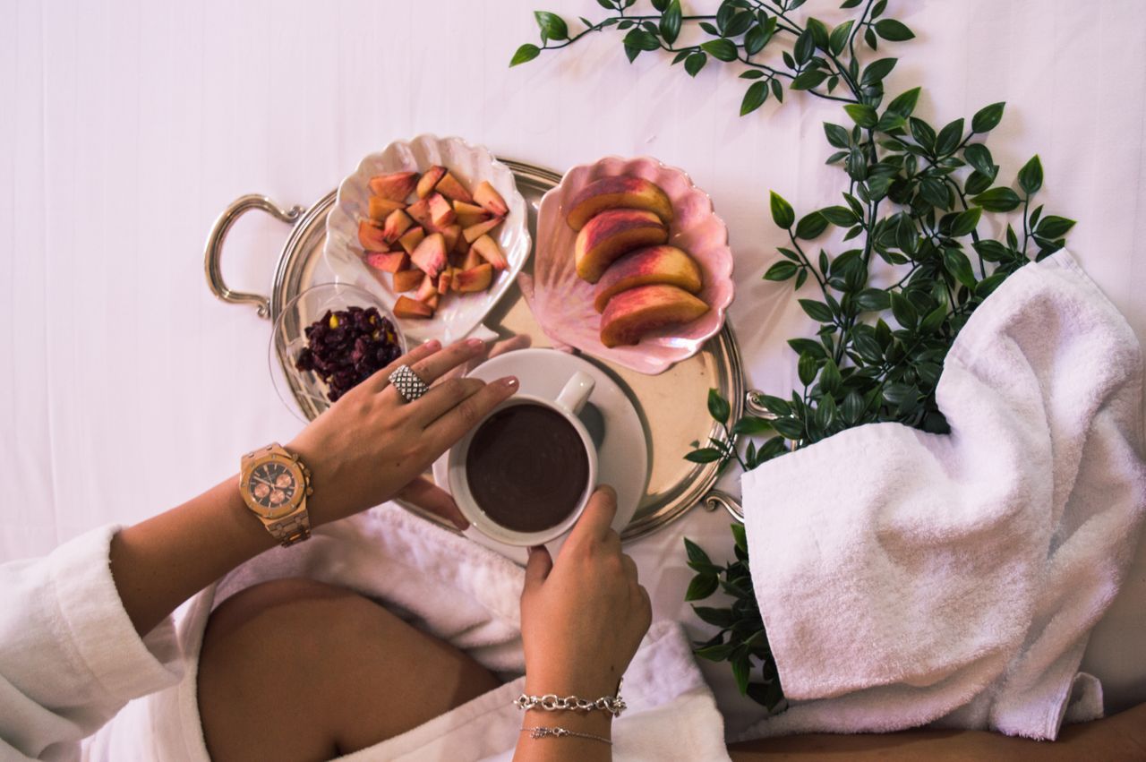 A woman’s hands reaching for a cup of coffee off of a tray, wearing jewelry and a watch