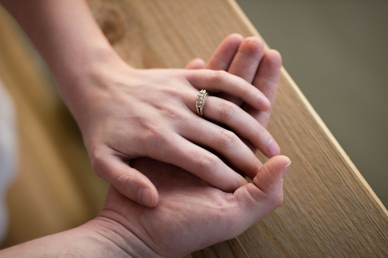A woman’s hand holding a man’s and wearing a yellow gold engagement ring