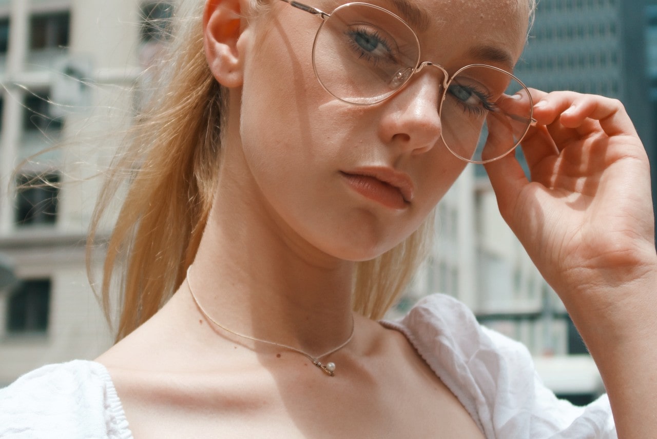A woman touching her glasses and a fine chain necklace featuring a pearl
