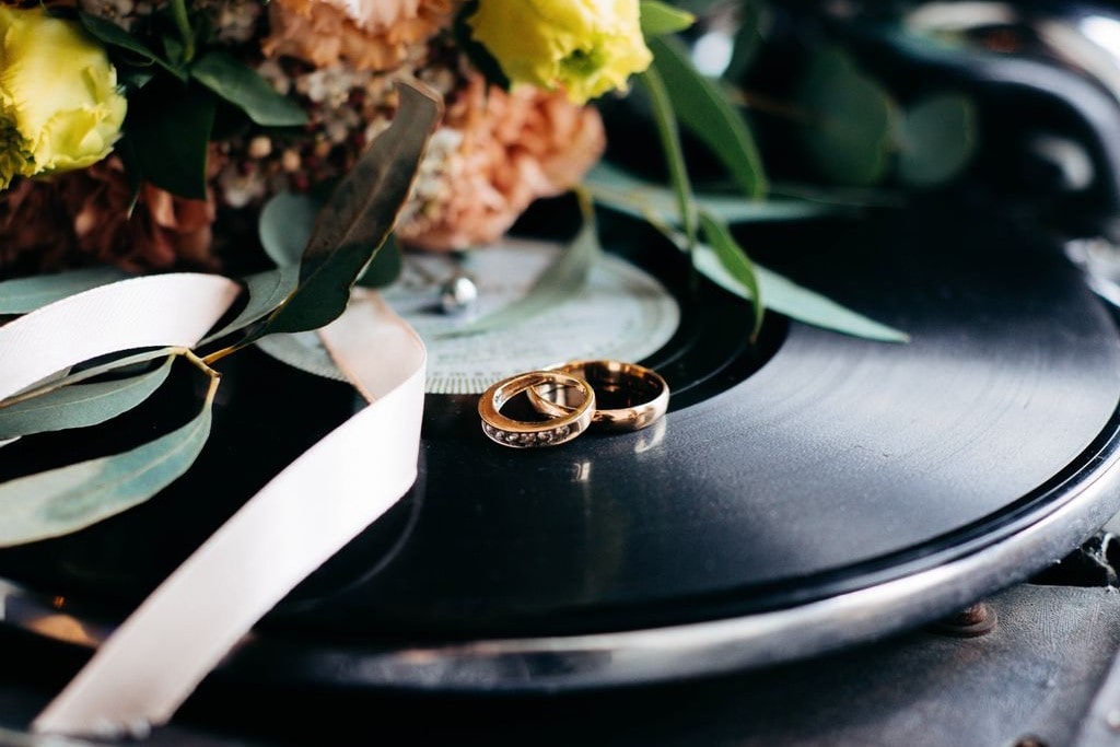 Two matching gold wedding rings displayed atop a turntable, a bouquet behind them.