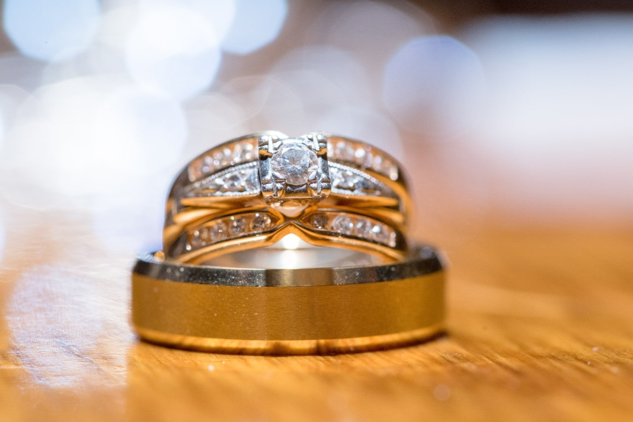 A close-up of a harmonious stack featuring two wedding bands and an engagement ring atop a wooden surface.