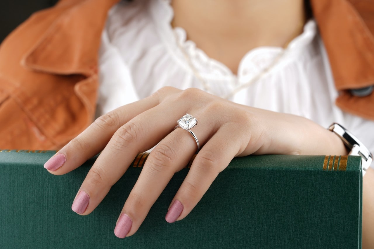 a woman grabbing a book wears a solitaire engagement ring.