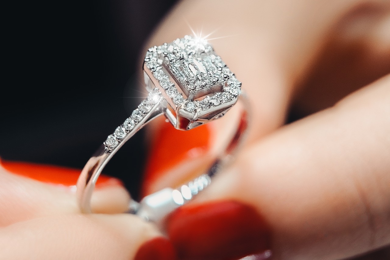 A woman holds an emerald-cut halo diamond ring.