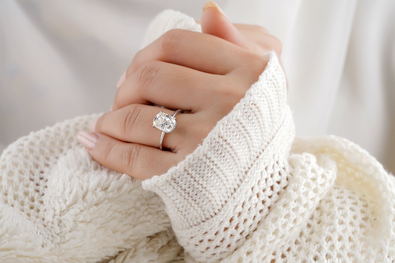 A woman snuggled up in a sweater wears a solitaire engagement ring.