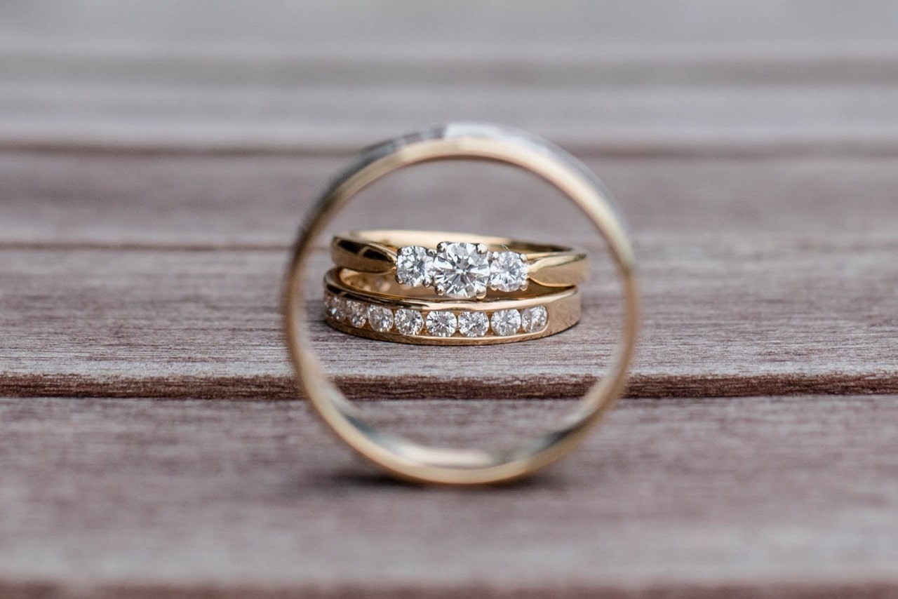 A yellow gold wedding band frames two yellow gold diamond studded rings on a rustic wooden surface.