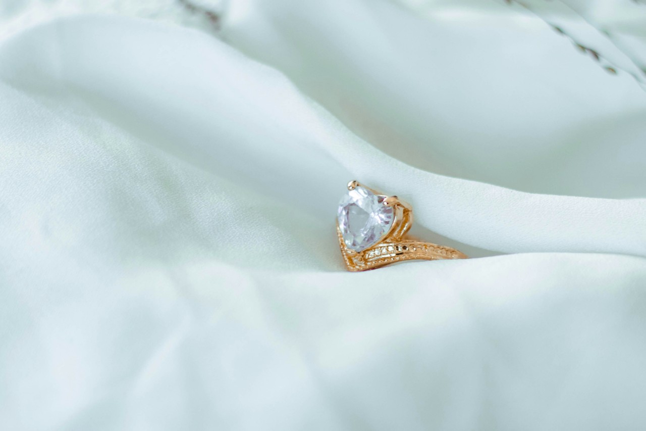 A diamond heart-shaped ring on a delicate, silky white cloth.
